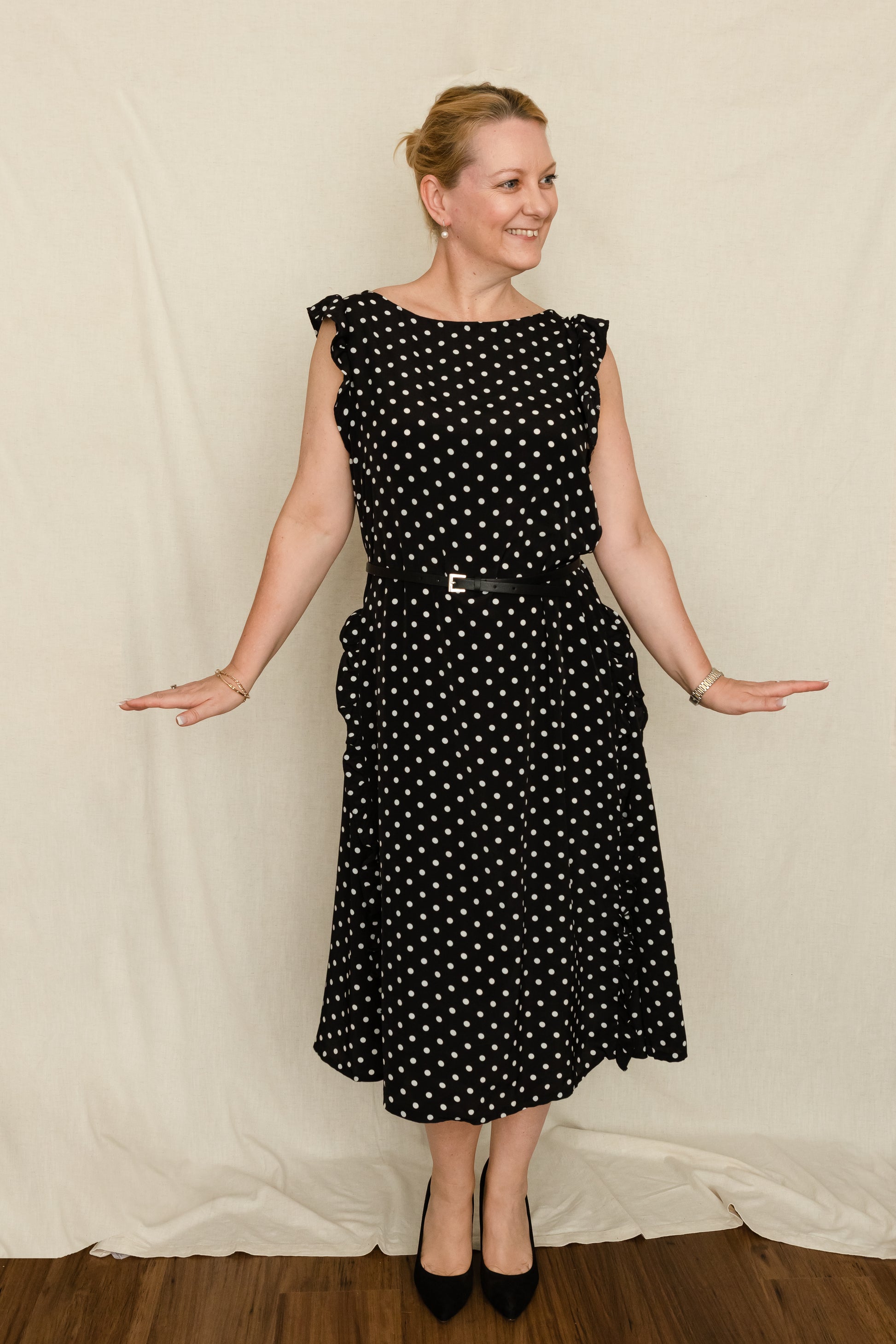 Woman wearing a 1920's vintage style dress with godets and ruffles in a black and white polka dot fabric, accessorised with a thin black belt.