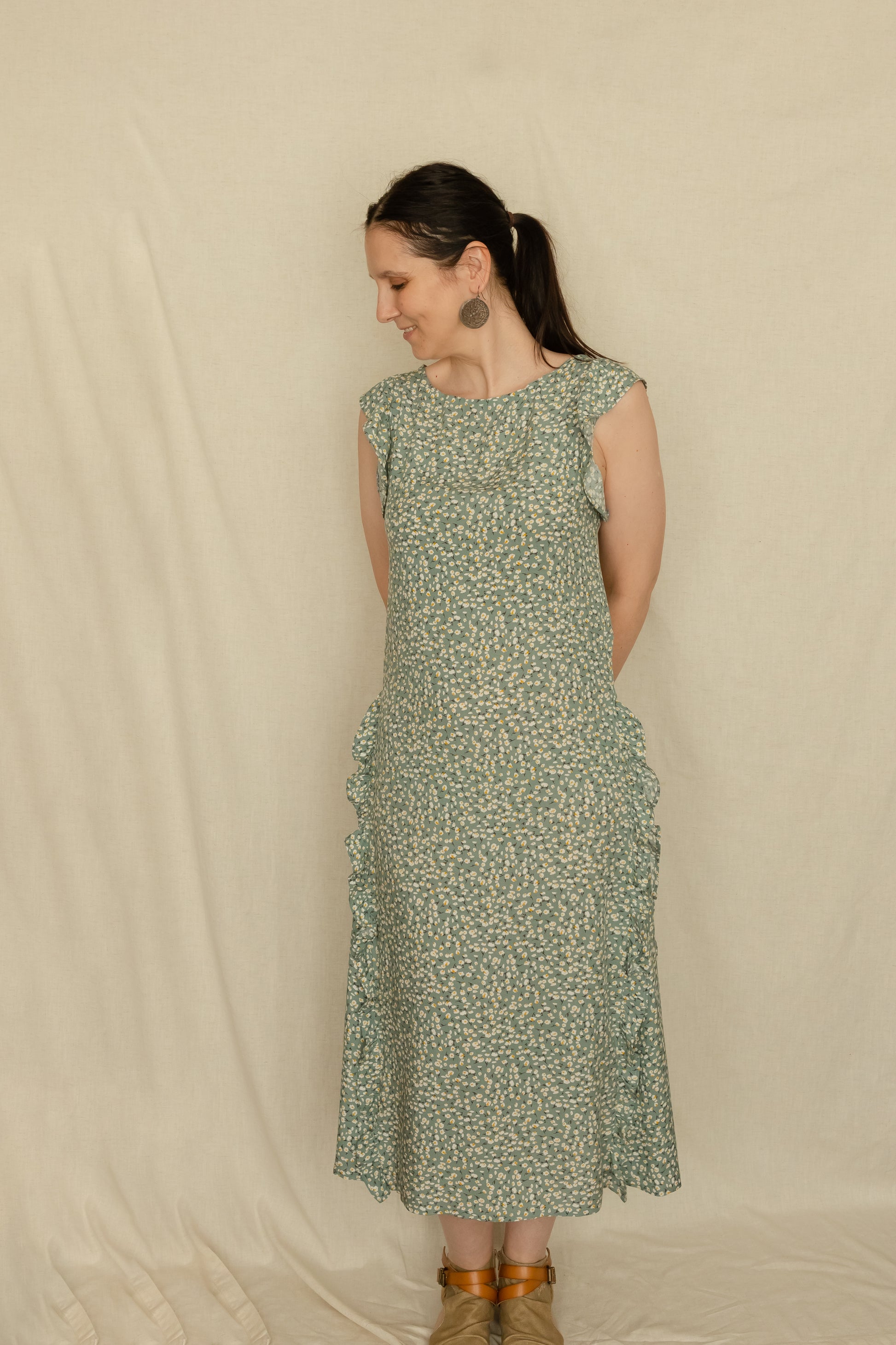 Woman standing with hands behind back whilst wearing a vintage inspired 1920's style dress featuring boho ruffles.