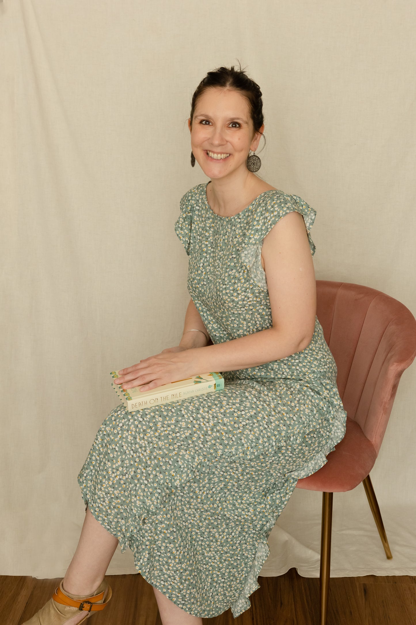 Woman sitting in a chair holding a book whilst wearing a 1920's vintage inspired dress featuring godets and ruffles.