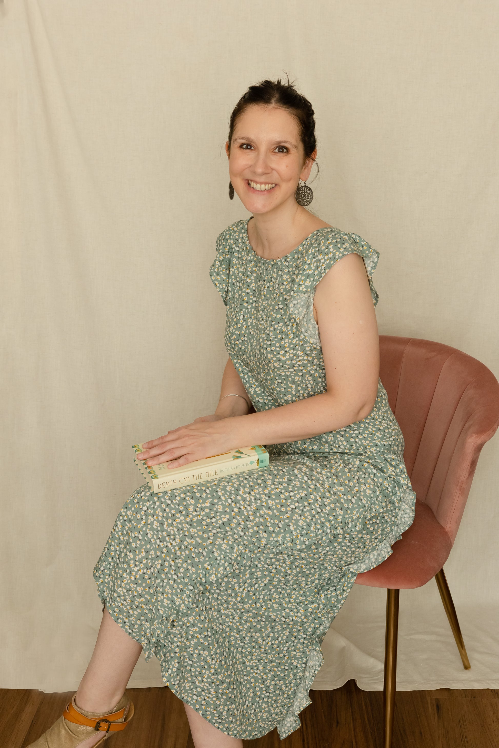 Woman sitting in a chair holding a book whilst wearing a 1920's vintage inspired dress featuring godets and ruffles.