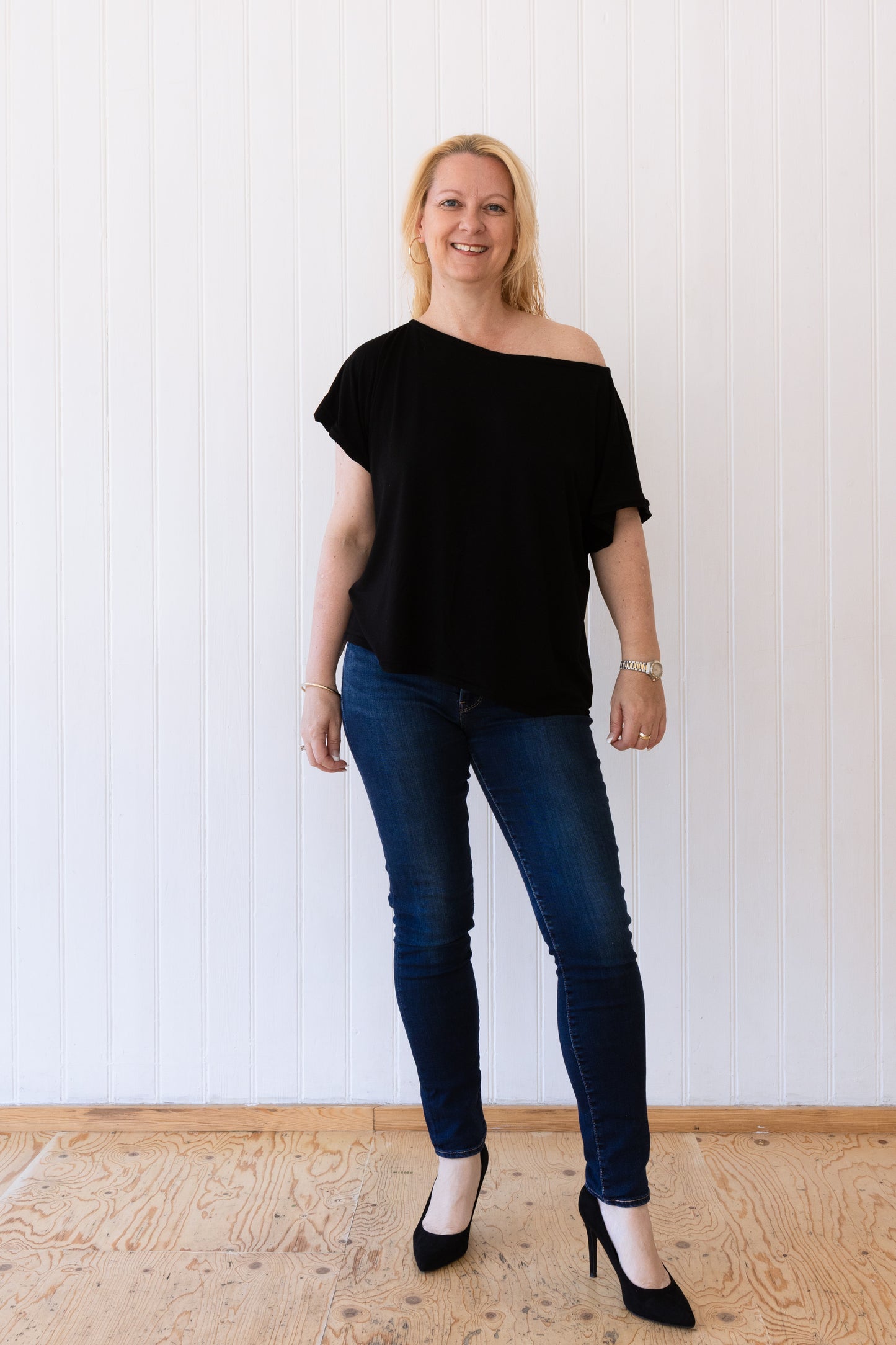 Woman in a black vintage inspired slouchy t-shirt draping off of one shoulder, worn with blue skinny jeans and high heels.