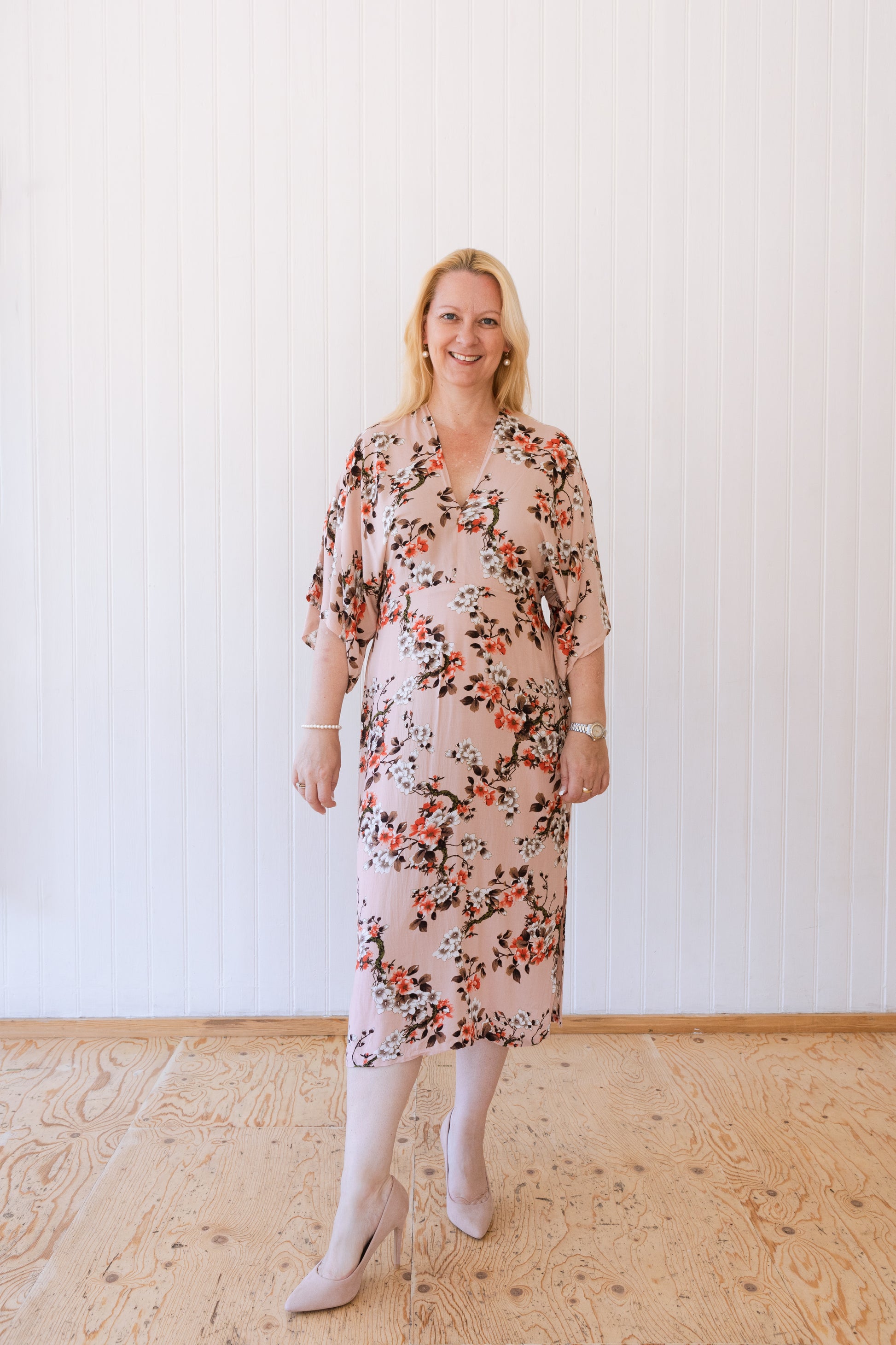 Woman wearing a vintage inspired summer dress with kimono sleeves in a soft peach fabric with foliage.