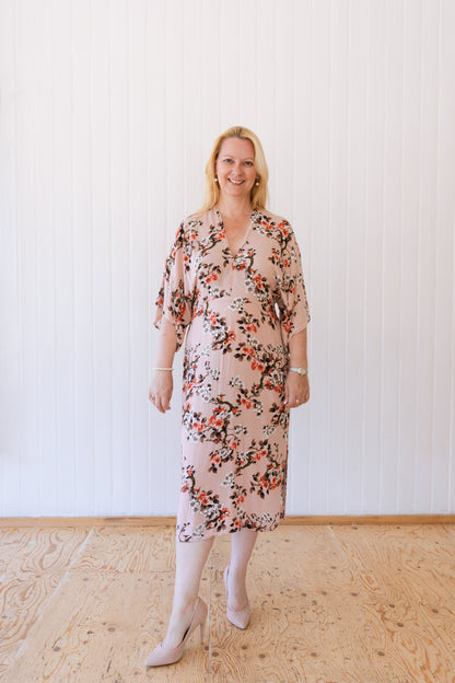 Woman wearing a vintage inspired summer dress with kimono sleeves in a soft peach fabric with foliage.
