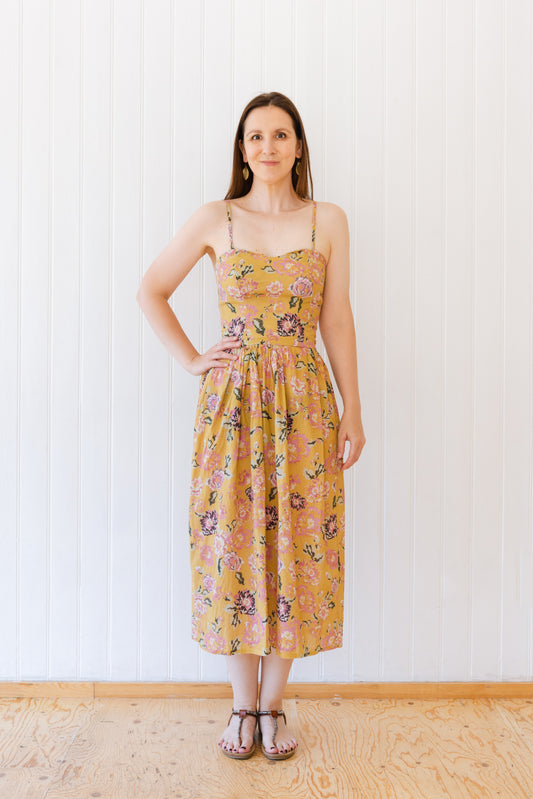 Woman wearing a vintage inspired midi length dress with a fitted princess seam bodice, gathered skirt and rouleau straps.