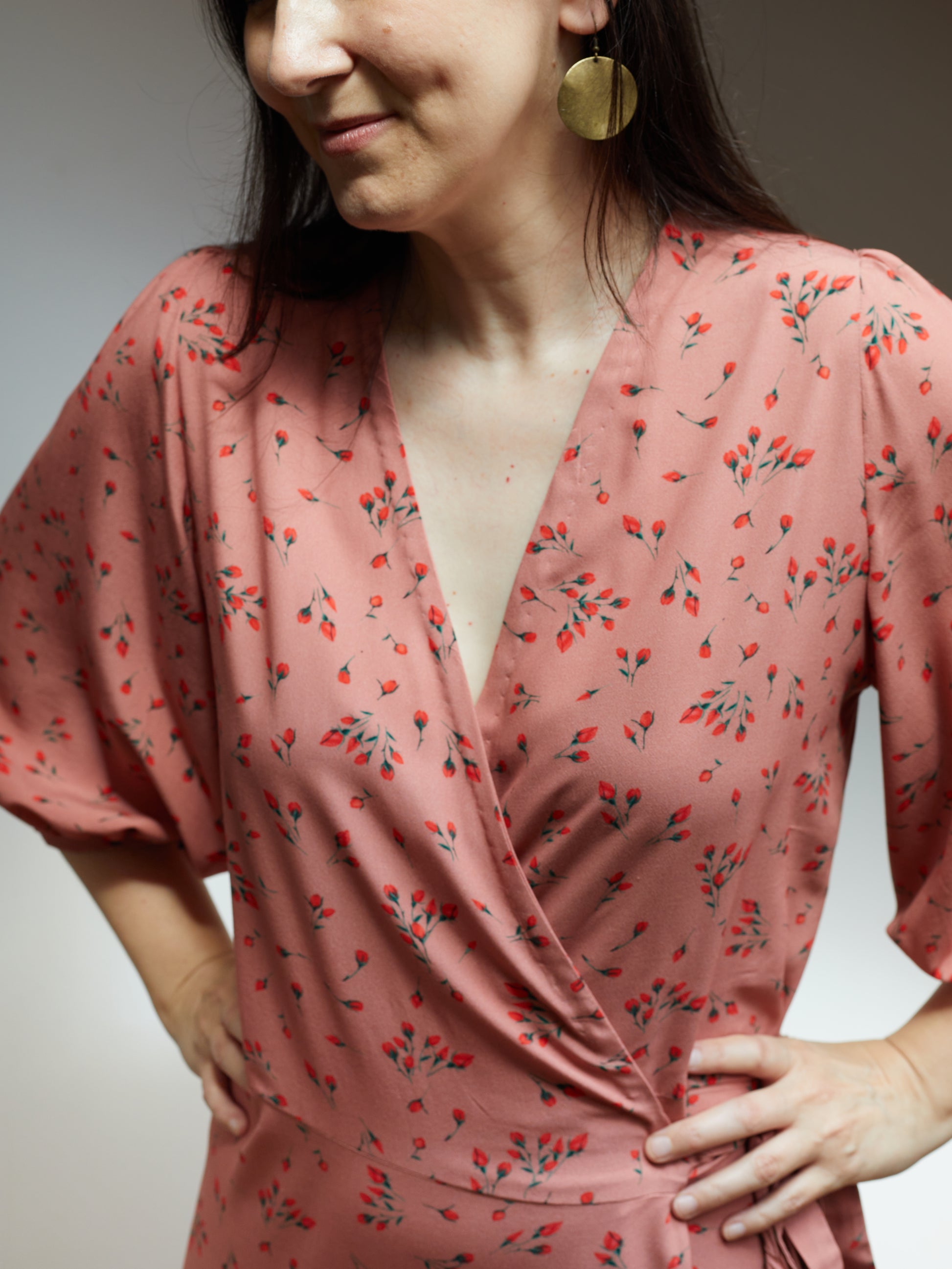 Close up of bodice of a wrap dress in a soft pink fabric with small red flowers.