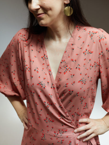 Close up of bodice of a wrap dress in a soft pink fabric with small red flowers.