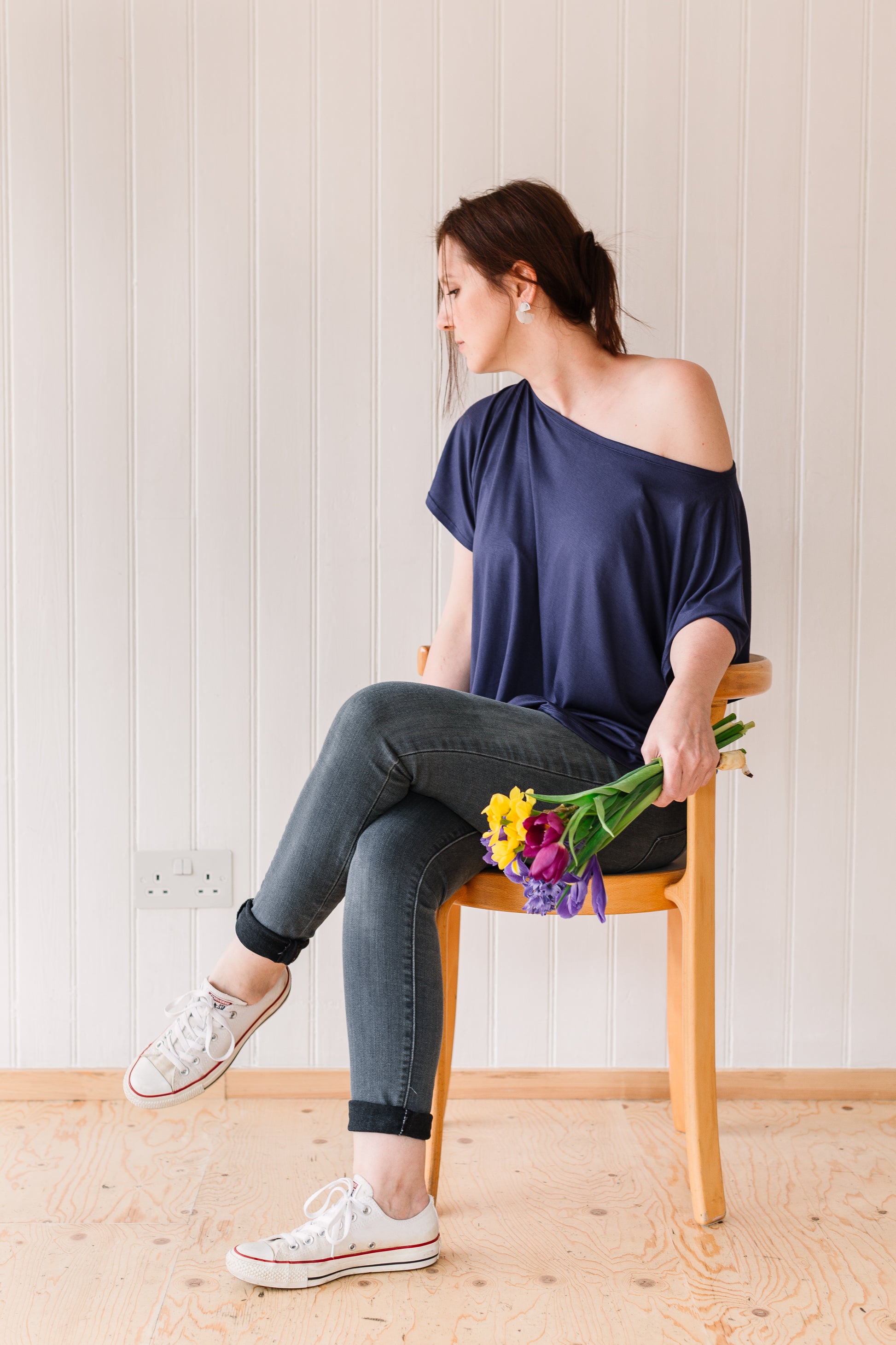 Woman sitting down wearing a vintage inspired off the shoulder slouchy t-shirt holding a bunch of flowers.