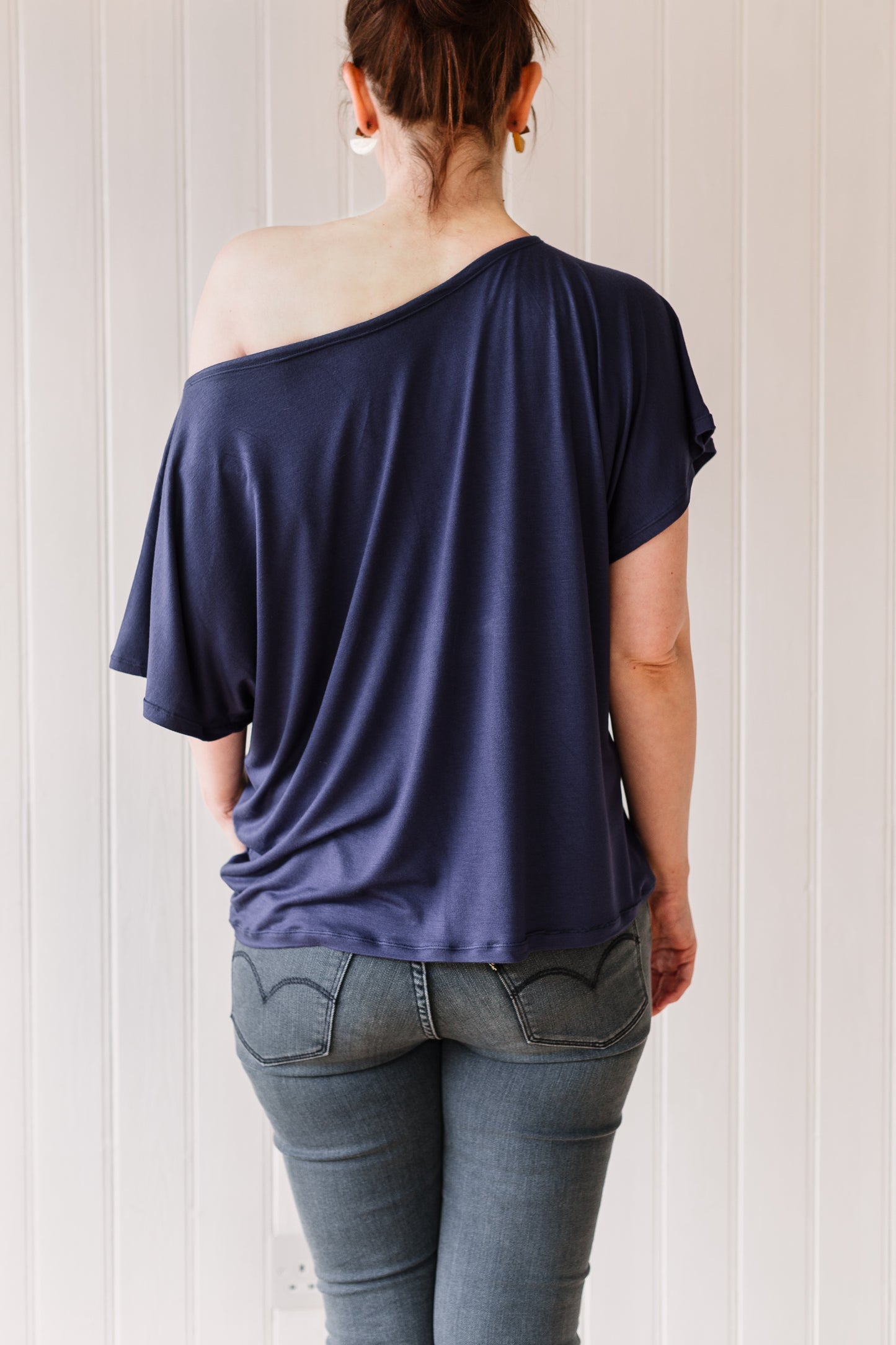 Back view of a woman wearing an off the shoulder, vintage inspired, slouchy t-shirt in a midnight blue colour.