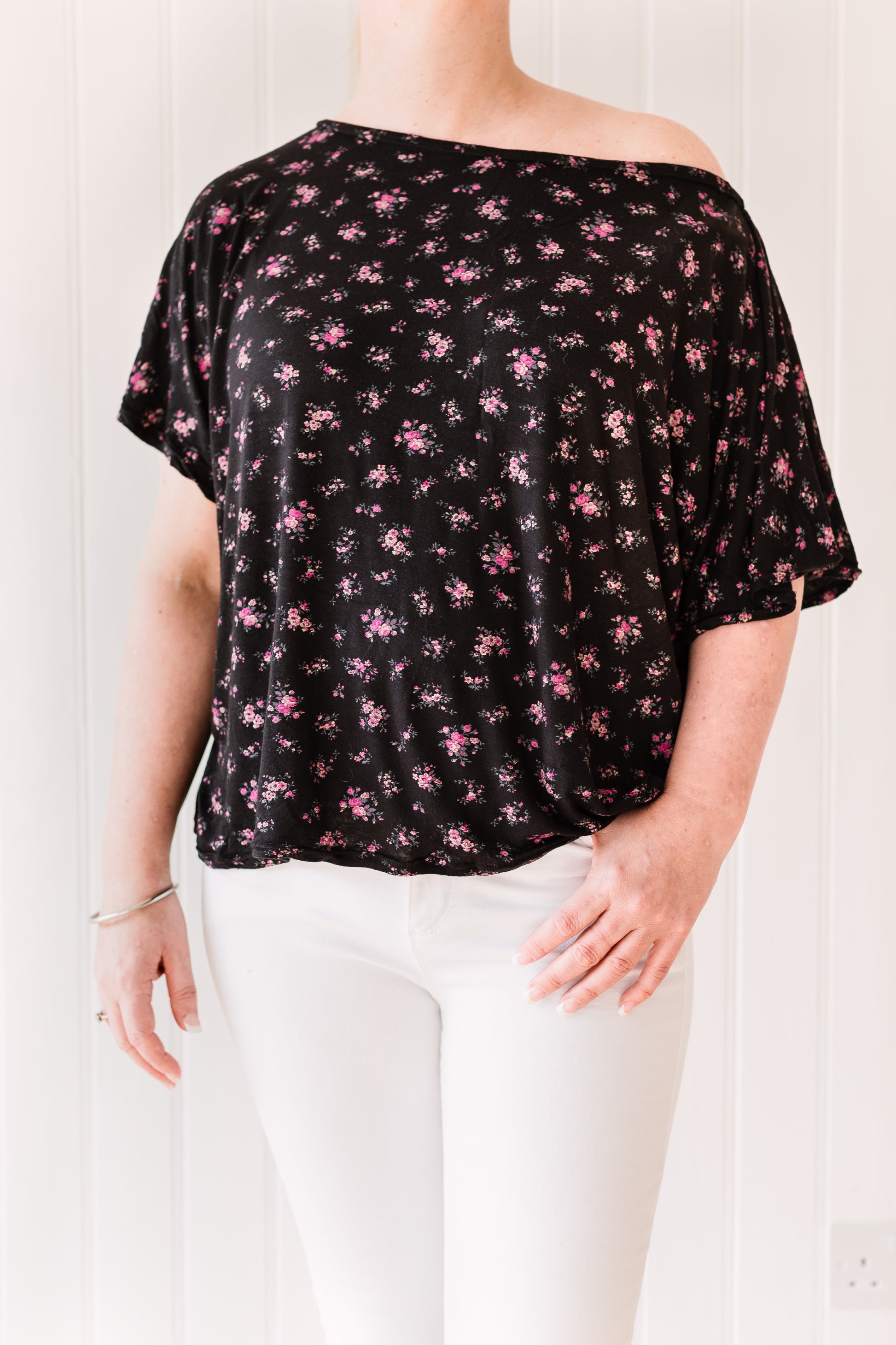 Woman wearing a vintage inspired slouchy, off the shoulder t-shirt in a black fabric with pink flowers.