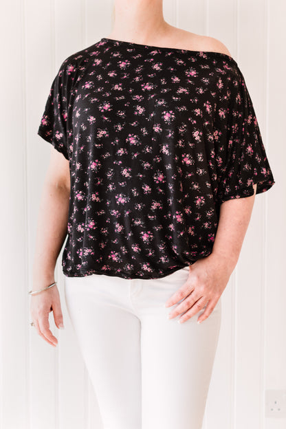 Woman wearing a vintage inspired slouchy, off the shoulder t-shirt in a black fabric with pink flowers.