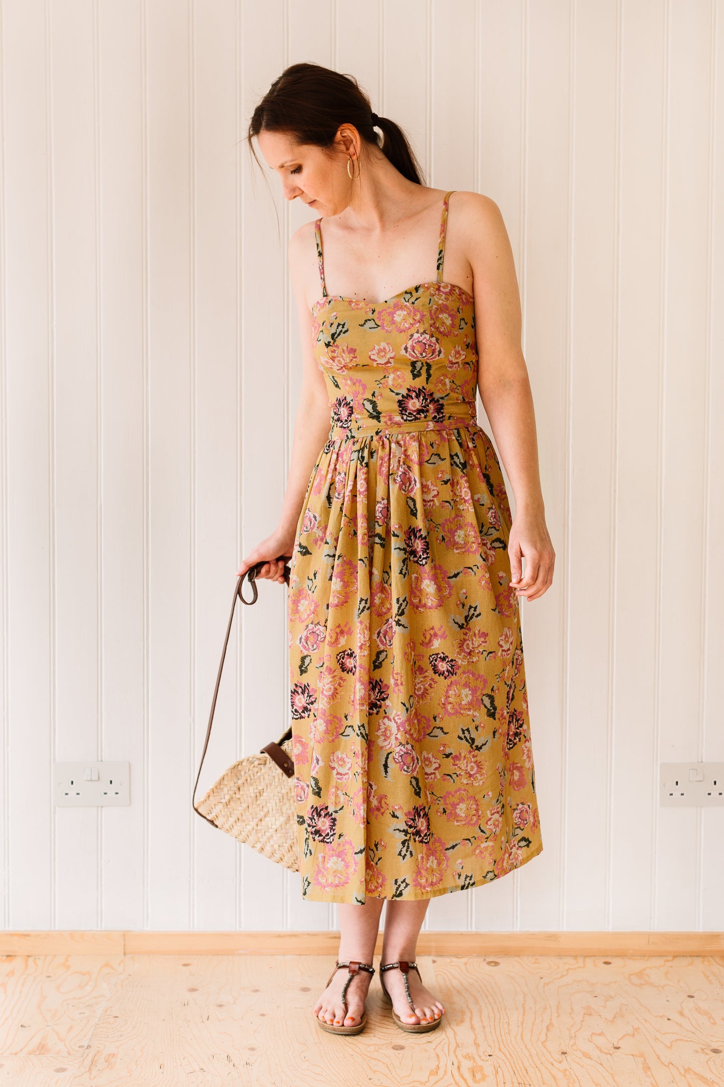 Midi length vintage inspired dress with a fitted bodice, gathered skirt and rouleau straps accessorised with straw bag.