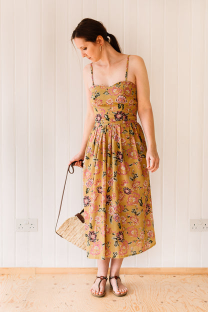 Midi length vintage inspired dress with a fitted bodice, gathered skirt and rouleau straps accessorised with straw bag.